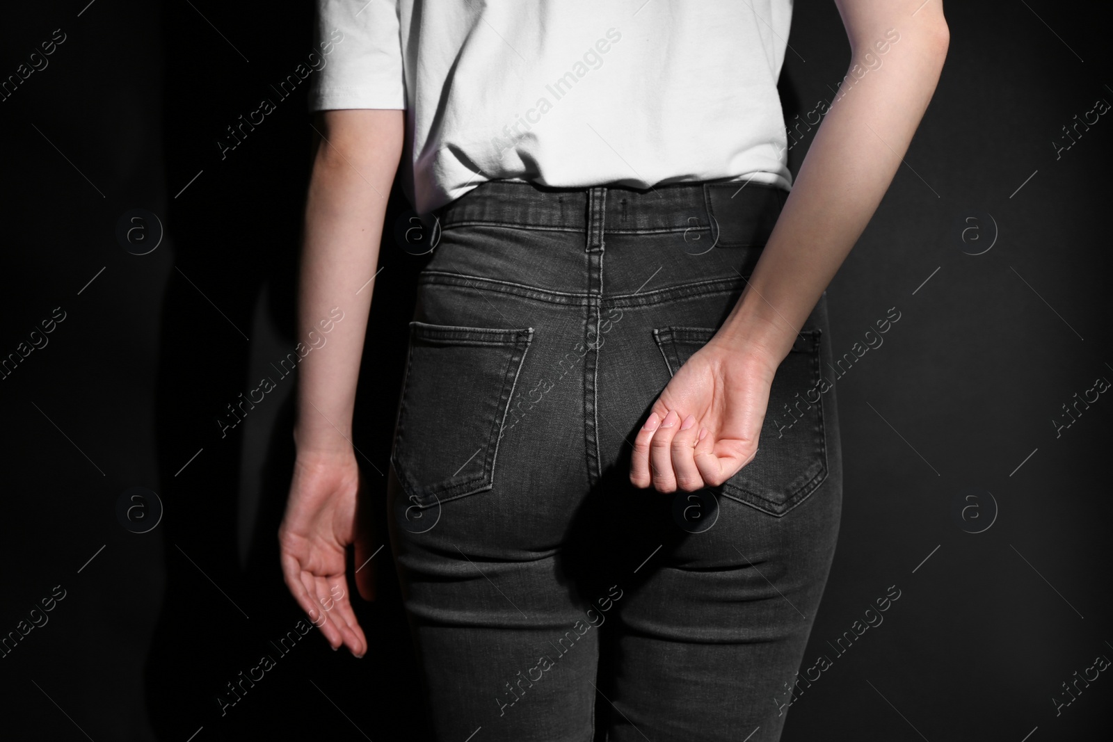 Photo of SOS gesture. Woman showing signal for help behind her back on black background, back view