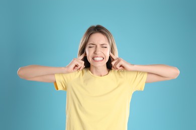 Photo of Emotional young woman covering her ears with fingers on light blue background