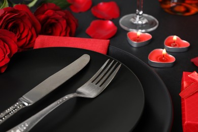 Photo of Dishware, cutlery, burning candles and bouquet on black table for romantic dinner, closeup