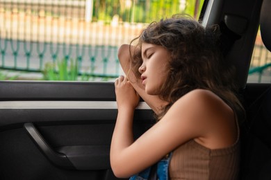 Photo of Tired girl with fastened seat belt sleeping in car