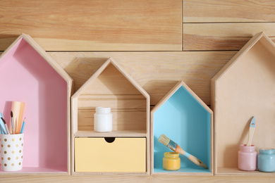 Photo of Painted house shaped shelves with different items on wooden wall. Interior elements