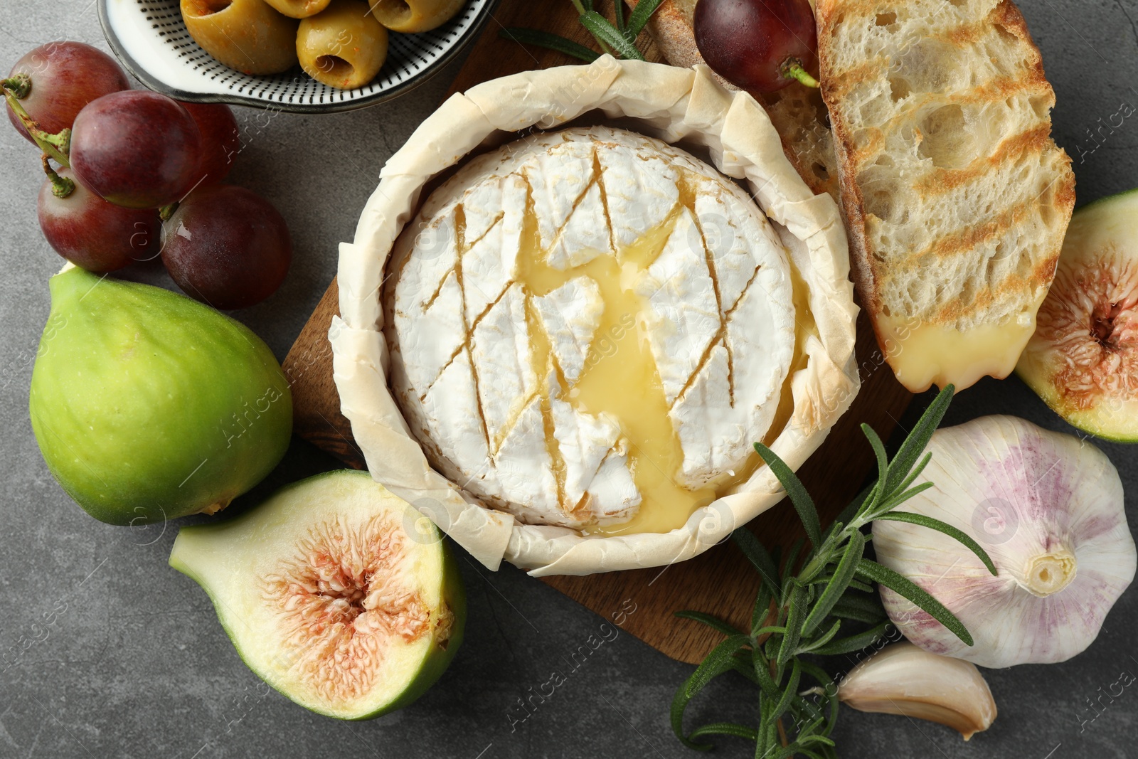 Photo of Tasty baked brie cheese and products on grey table, flat lay