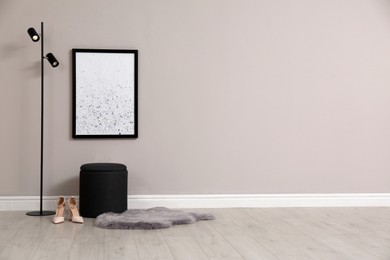 Stylish pouf, lamp, shoes and faux fur near beige wall indoors. Space for text