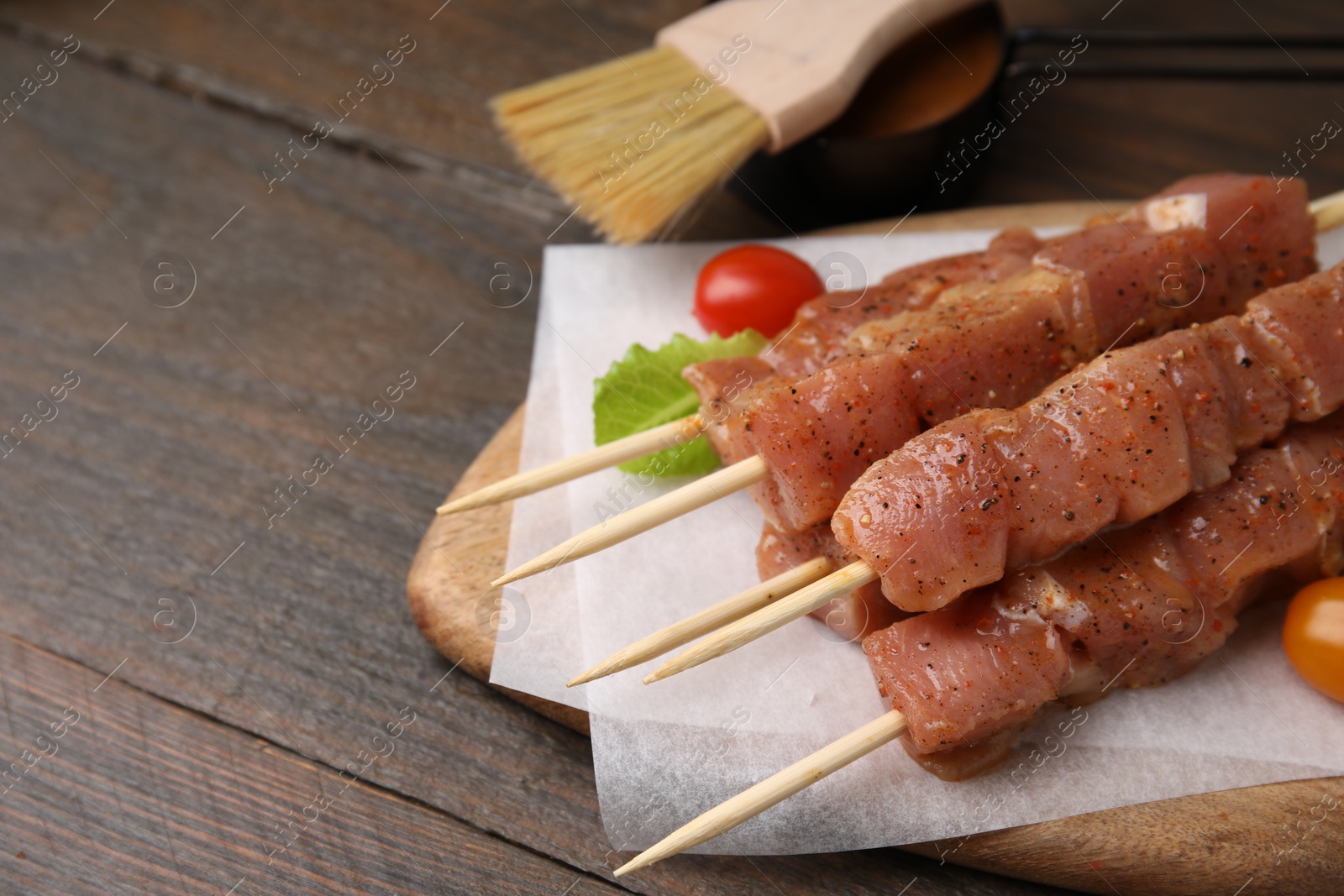 Photo of Skewers with cut raw marinated meat on wooden table. Space for text