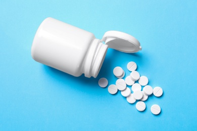 Photo of Pills and bottle on light blue background, top view