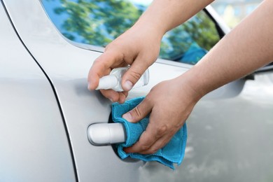 Photo of Man with duster and spray sanitizing car door handle outdoors, closeup