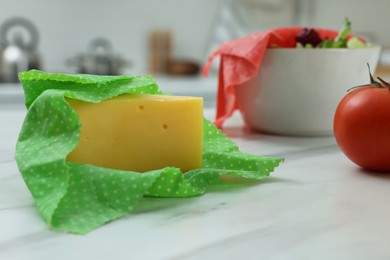 Photo of Piece of cheese in beeswax food wrap on white marble table