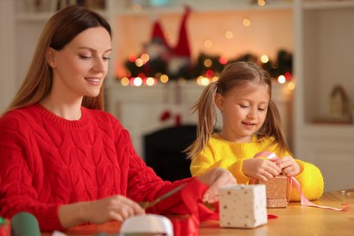 Photo of Christmas presents wrapping. Mother and her little daughter decorating gift boxes with ribbon at home, selective focus