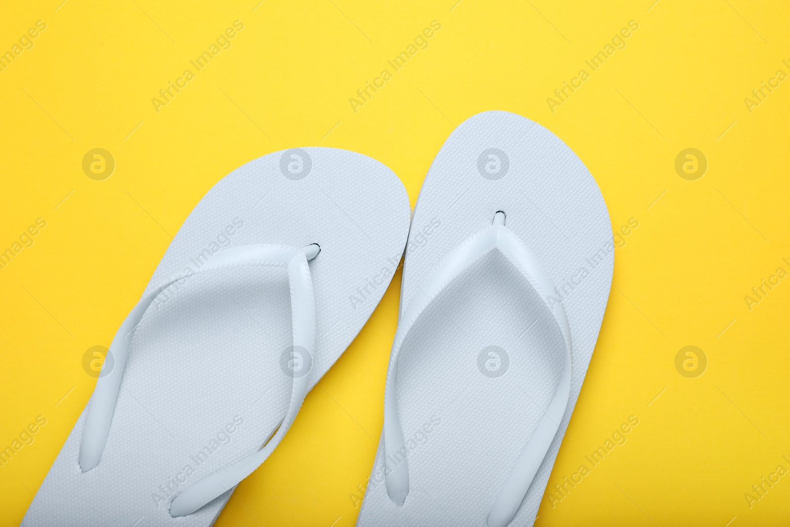 Photo of Stylish white flip flops on yellow background, top view