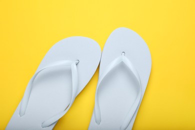 Stylish white flip flops on yellow background, top view