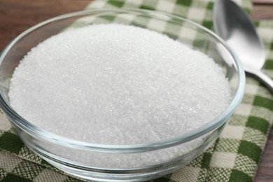 Photo of Granulated sugar in bowl and napkin on table, closeup