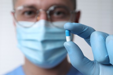 Doctor holding pill on light background, selective focus. Space for text