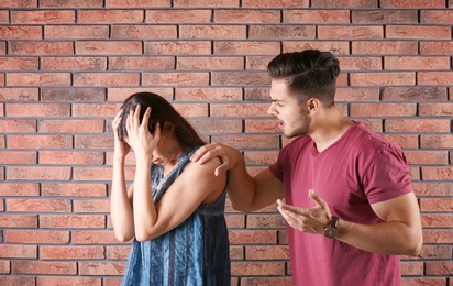 Photo of Young couple having argument near brick wall. Relationship problems
