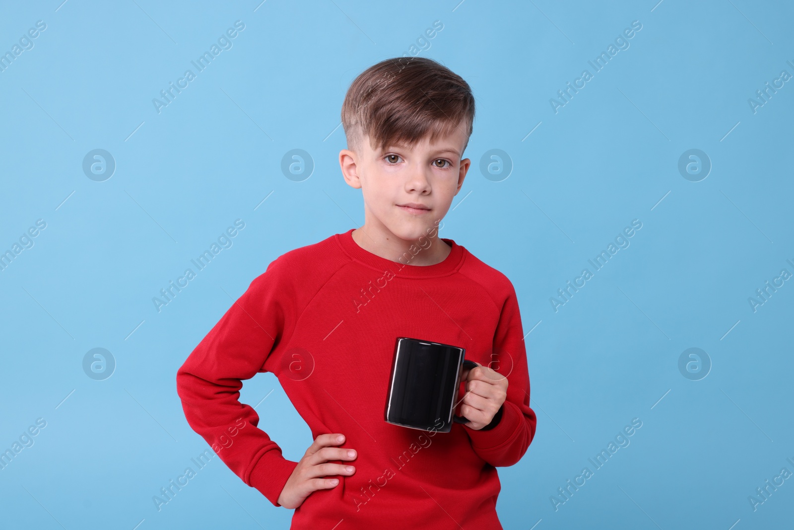 Photo of Cute boy with black ceramic mug on light blue background