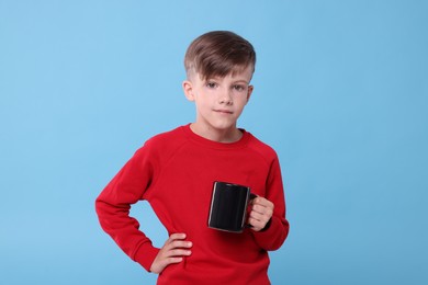 Photo of Cute boy with black ceramic mug on light blue background