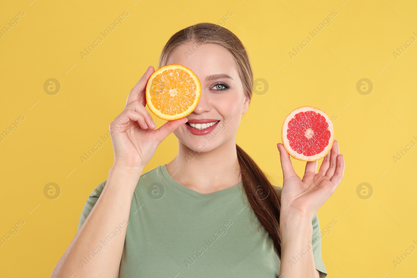 Photo of Young woman with cut orange and grapefruit on yellow background. Vitamin rich food