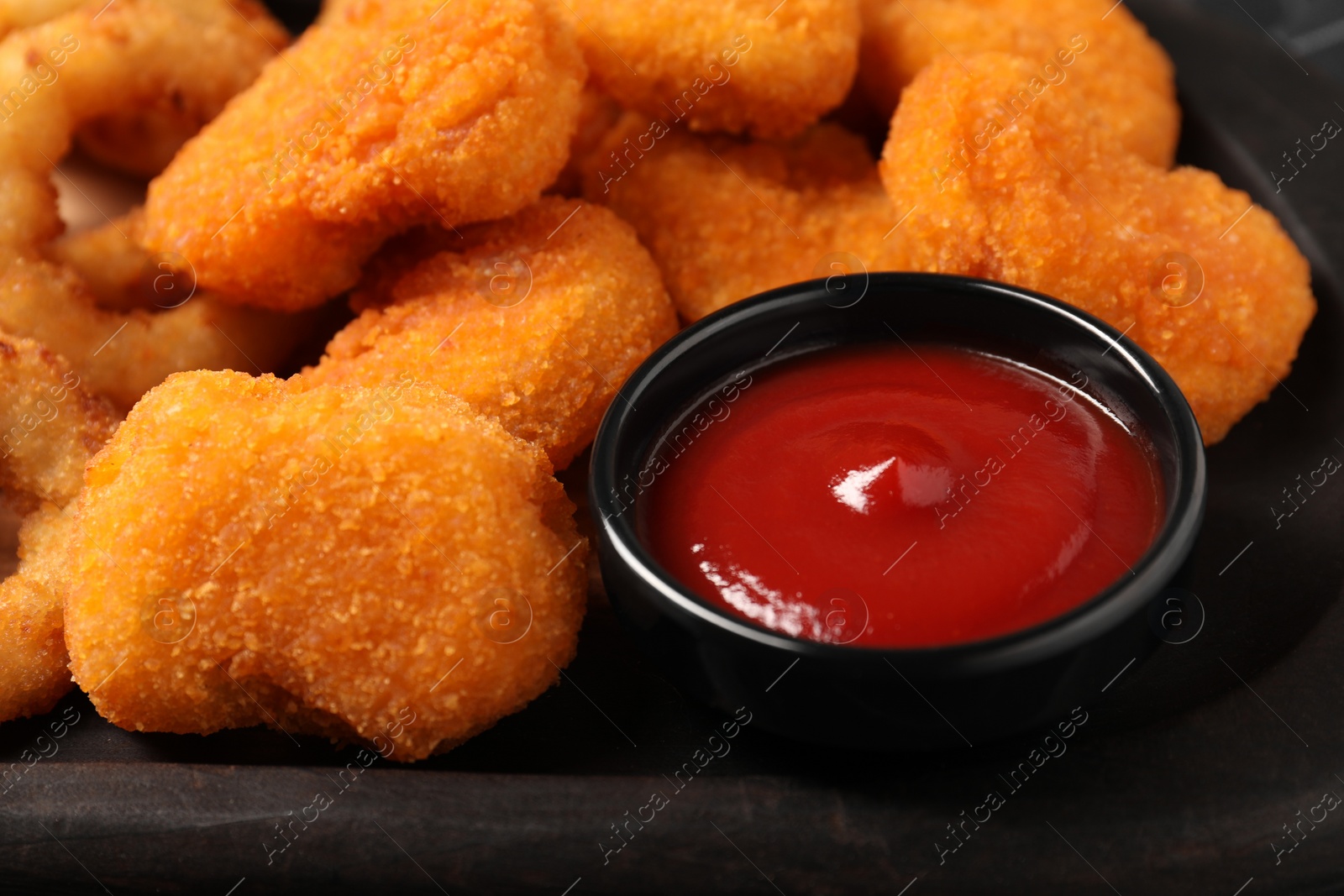 Photo of Tasty ketchup and chicken nuggets on black plate, closeup