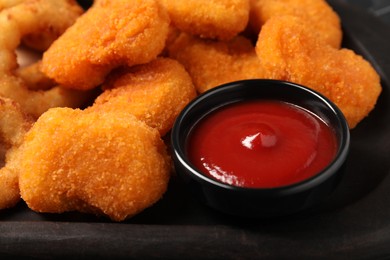 Tasty ketchup and chicken nuggets on black plate, closeup