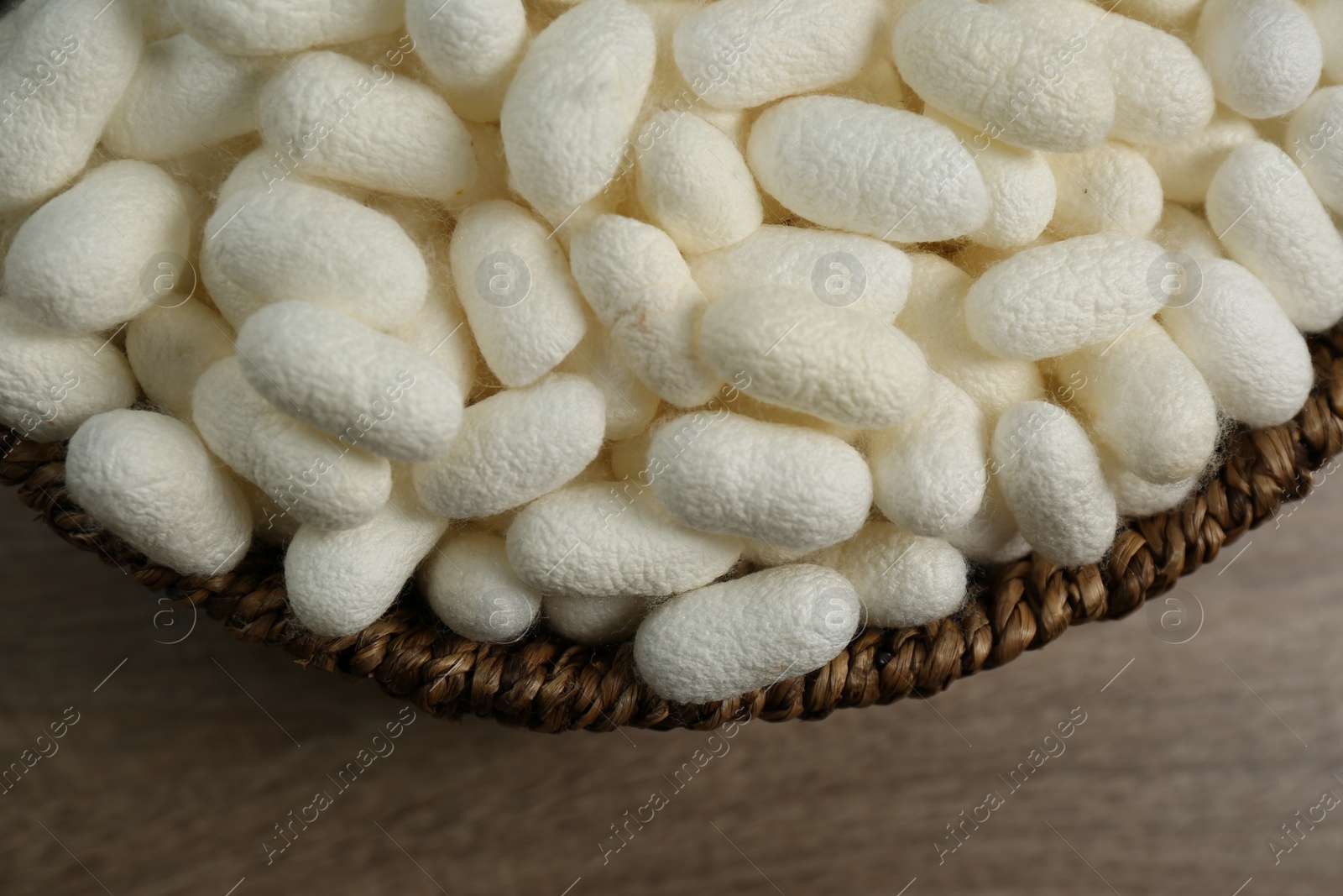 Photo of White silk cocoons in bowl on wooden table, closeup