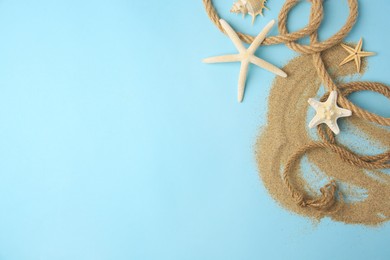 Photo of Beautiful sea stars, rope and sand on light blue background, flat lay. Space for text