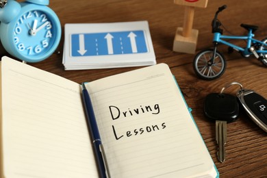 Photo of Workbook for driving lessons, pen and car key on wooden table, closeup. Passing license exam