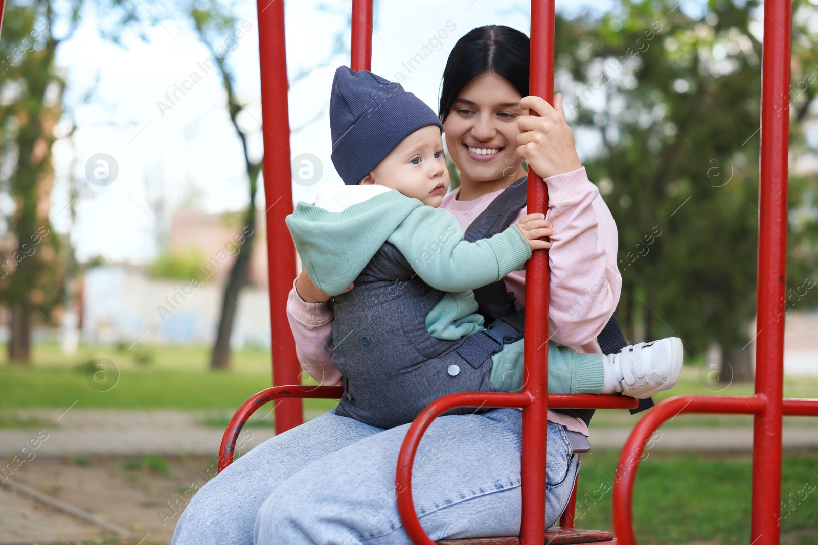 Photo of Mother holding her child in sling (baby carrier) on swing outdoors