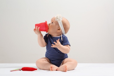 Photo of Little girl with sippy cup and toy carrot on light background. Baby accessories