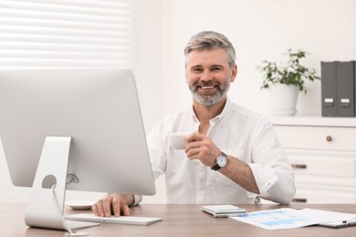 Photo of Professional accountant with cup of coffee working at wooden desk in office