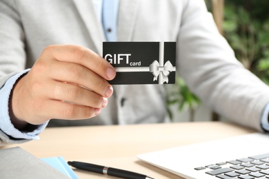 Man with gift card and laptop at table indoors, closeup