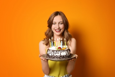 Young woman with birthday cake on color background