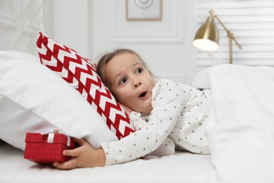 Photo of Excited little girl finding gift box under pillow in bed at home. Saint Nicholas day tradition