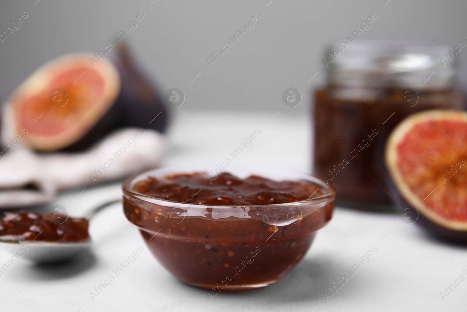 Photo of Tasty sweet fig jam and fruits on white marble table, closeup