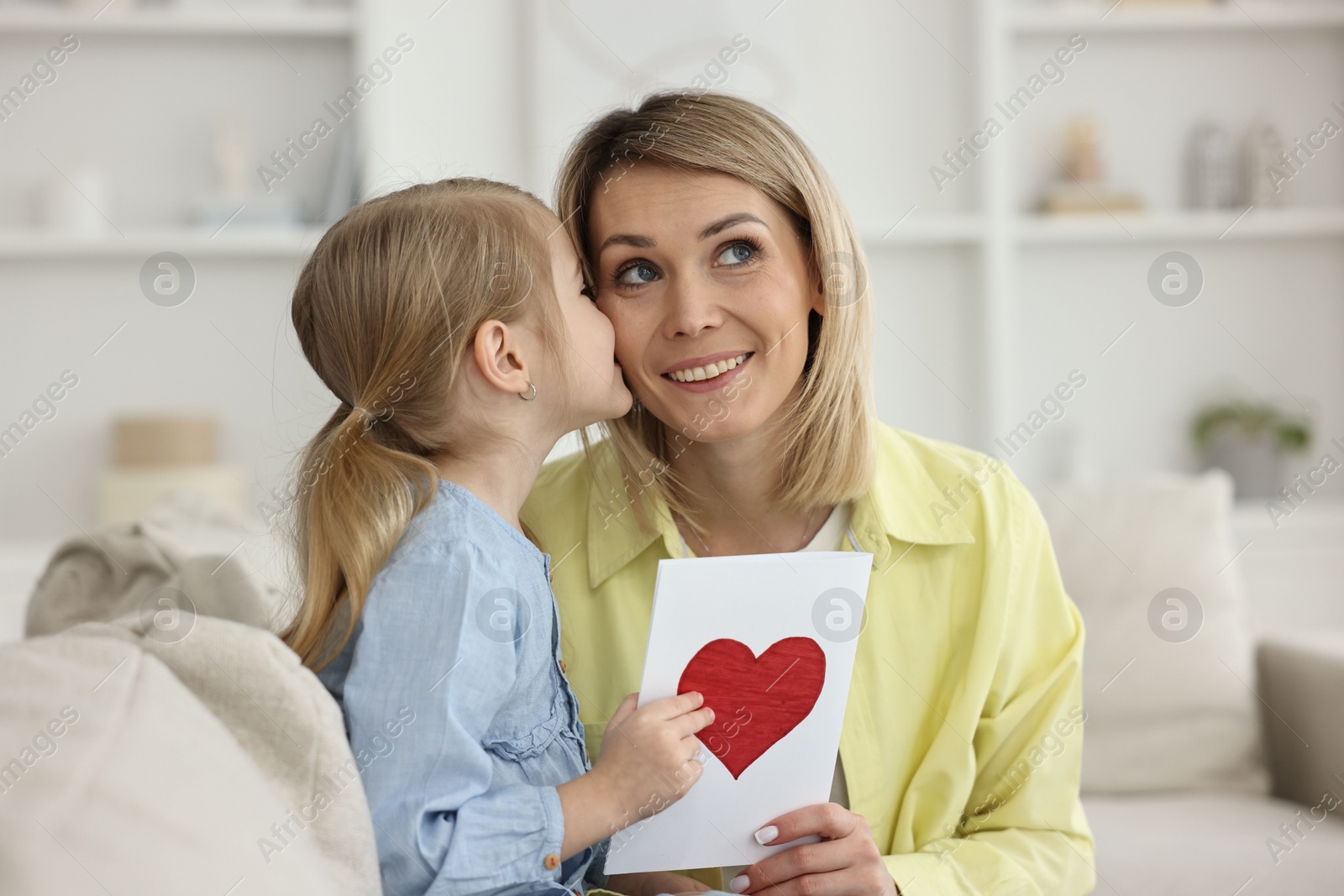 Photo of Little daughter kissing and congratulating her mom with greeting card at home. Happy Mother's Day