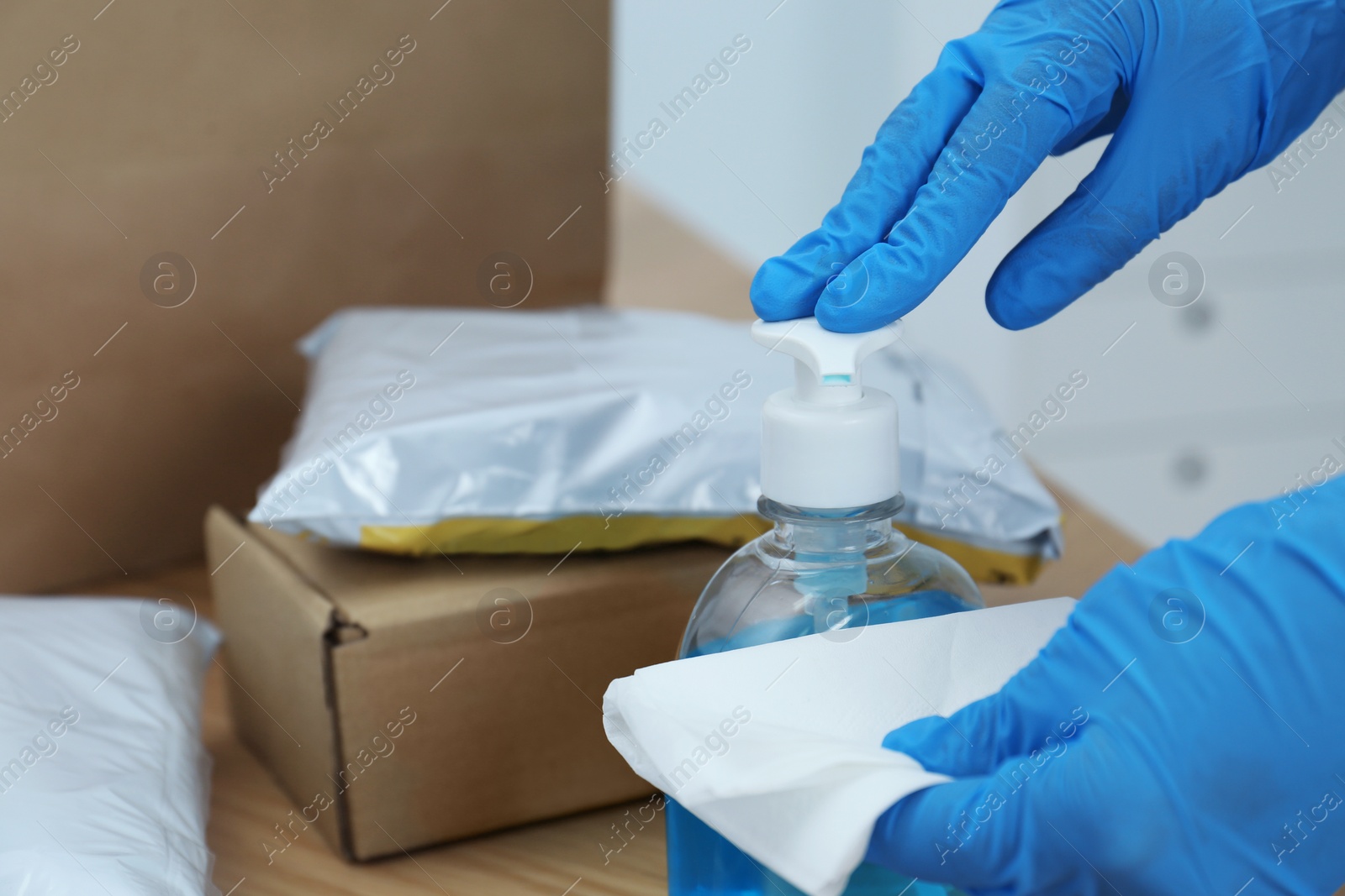 Photo of Woman applying antiseptic gel onto wipe while cleaning parcels at table, closeup. Preventive measure during COVID-19 pandemic