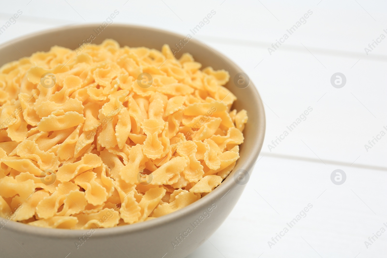 Photo of Raw farfalline pasta in bowl on white table, closeup. Space for text