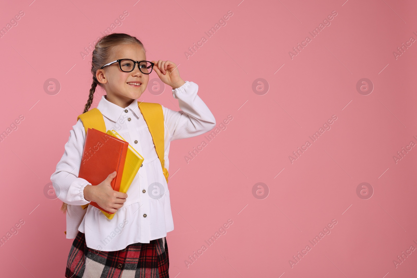Photo of Happy schoolgirl with backpack and books on pink background, space for text
