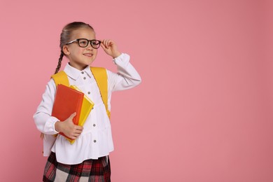 Happy schoolgirl with backpack and books on pink background, space for text