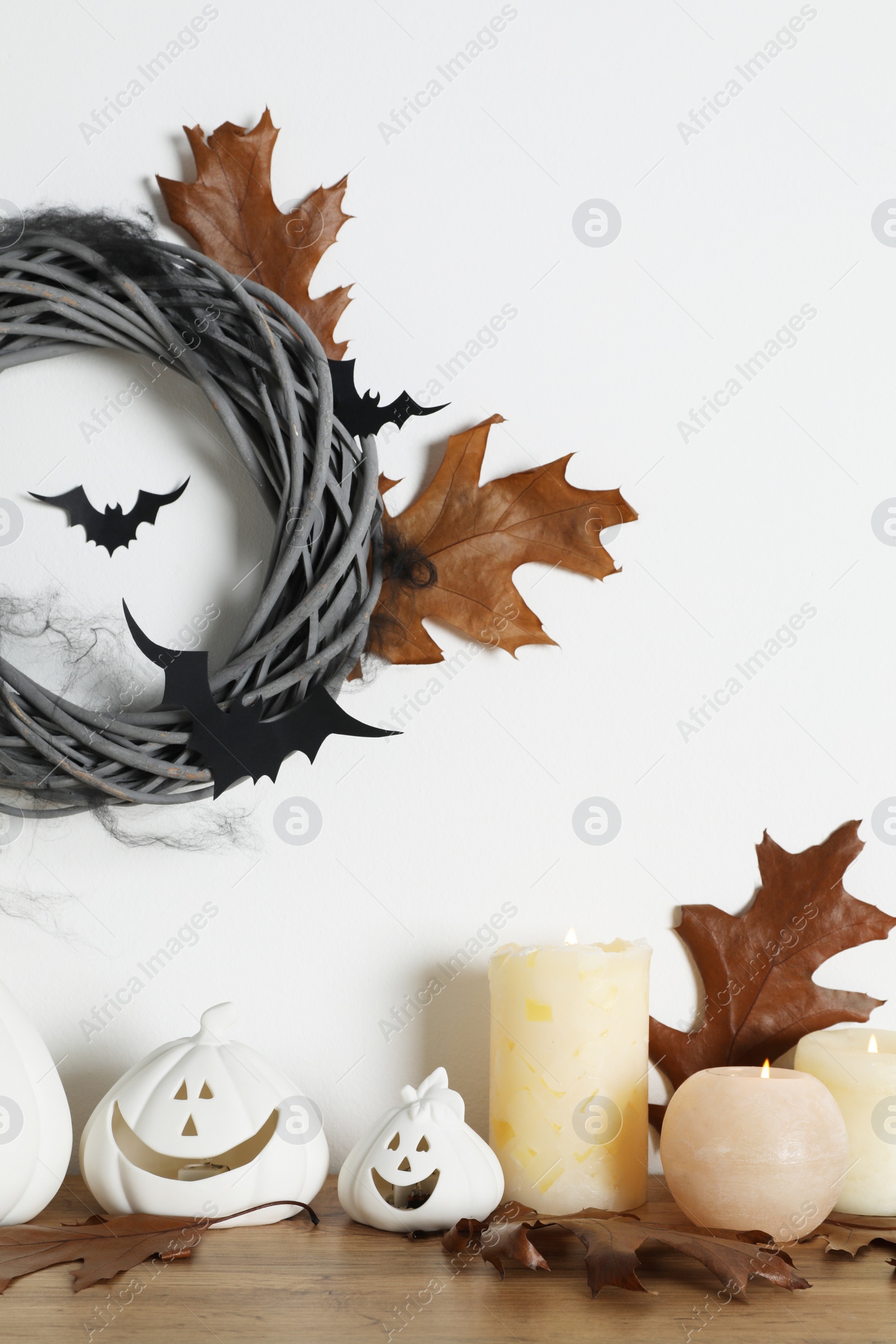 Photo of Different pumpkin shaped holders, autumn leaves and burning candles on wooden table. Halloween decor