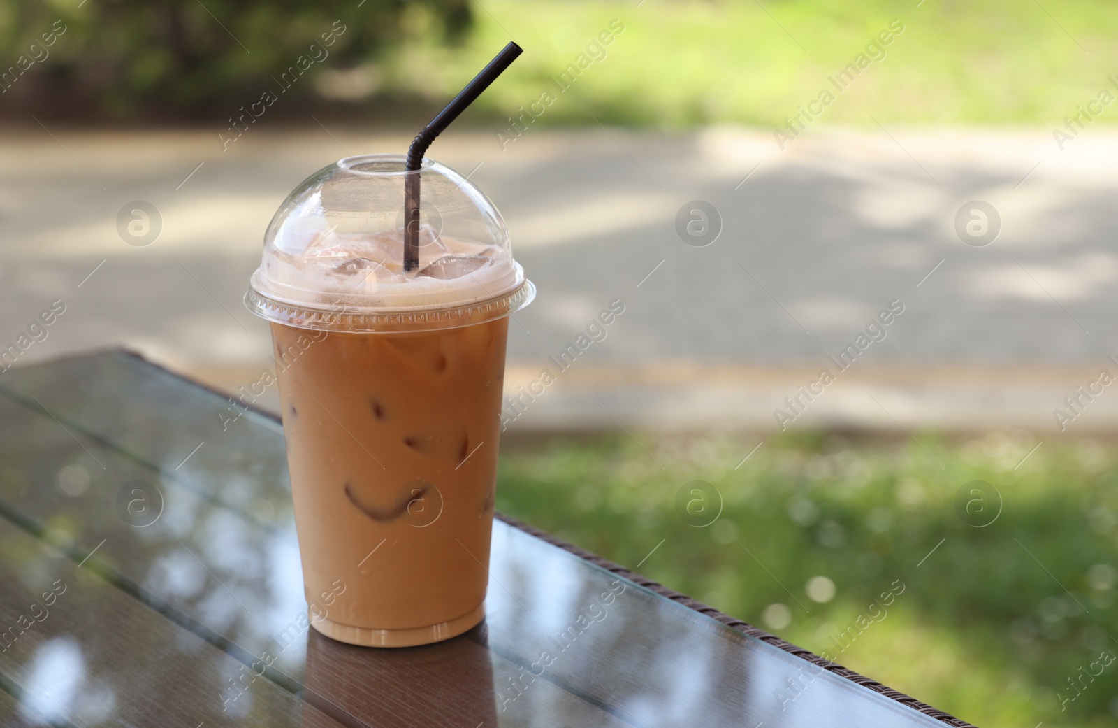 Photo of Plastic takeaway cup of delicious iced coffee on table in outdoor cafe, space for text