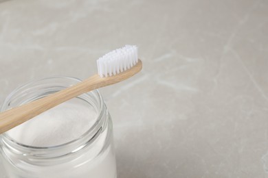 Bamboo toothbrush and jar of baking soda on light marble table, space for text