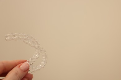 Photo of Woman with transparent dental aligners on beige background, closeup. Space for text