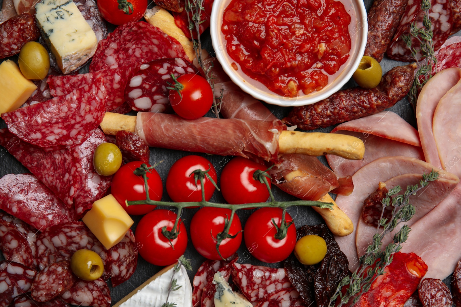 Photo of Tasty ham with other delicacies on black table, flat lay