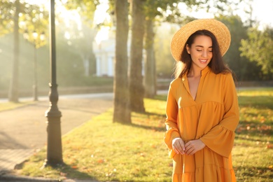 Beautiful young woman wearing stylish yellow dress and straw hat in park