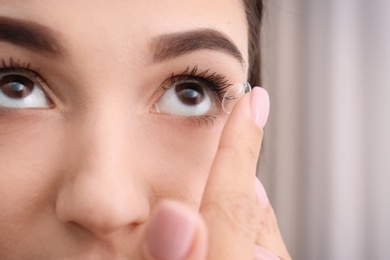 Photo of Young woman putting contact lens in her eye, closeup