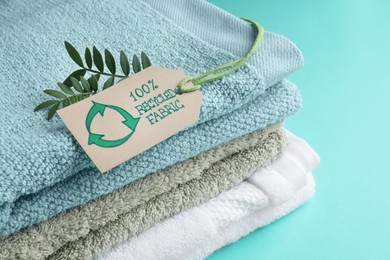Photo of Stacked towels with recycling label and plant on turquoise background, closeup