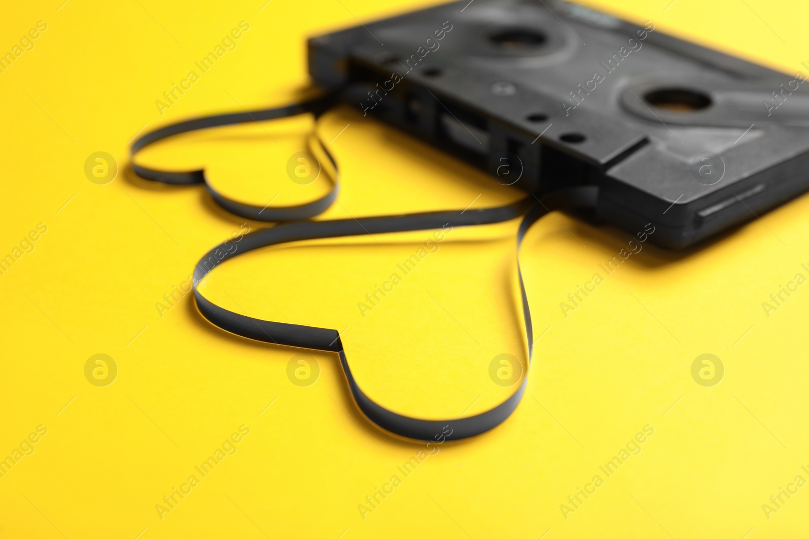 Photo of Music cassette and hearts made with tape on yellow background, closeup. Listening love song