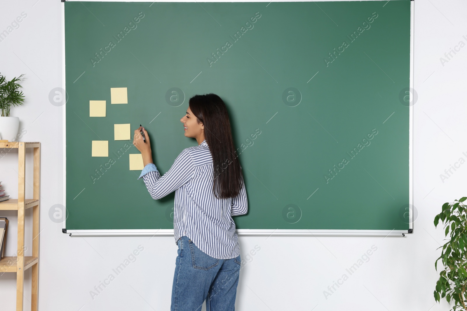 Photo of Happy young teacher giving lesson at blackboard in classroom. Space for text