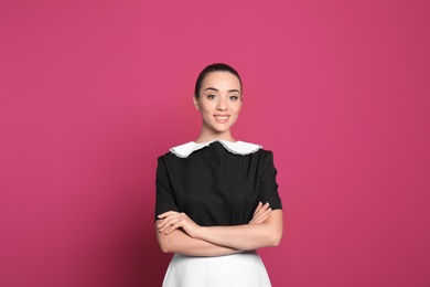 Portrait of young chambermaid in tidy uniform on color background