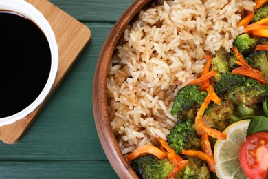 Tasty fried rice with vegetables served on green wooden table, flat lay