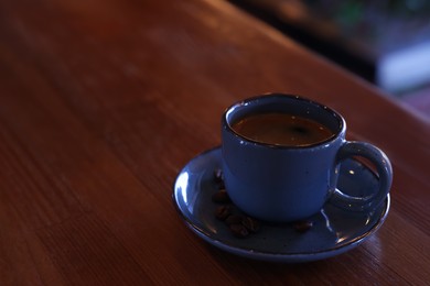 Photo of Cup of hot aromatic coffee and roasted beans on wooden table in cafe. Space for text